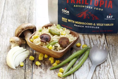 Adventure food package with prepared ramen noodles in bowl alongside fresh vegetables and spoon