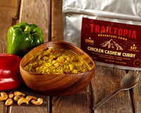 Adventure food pouch with prepared curry dish in wooden bowl surrounded by fresh ingredients