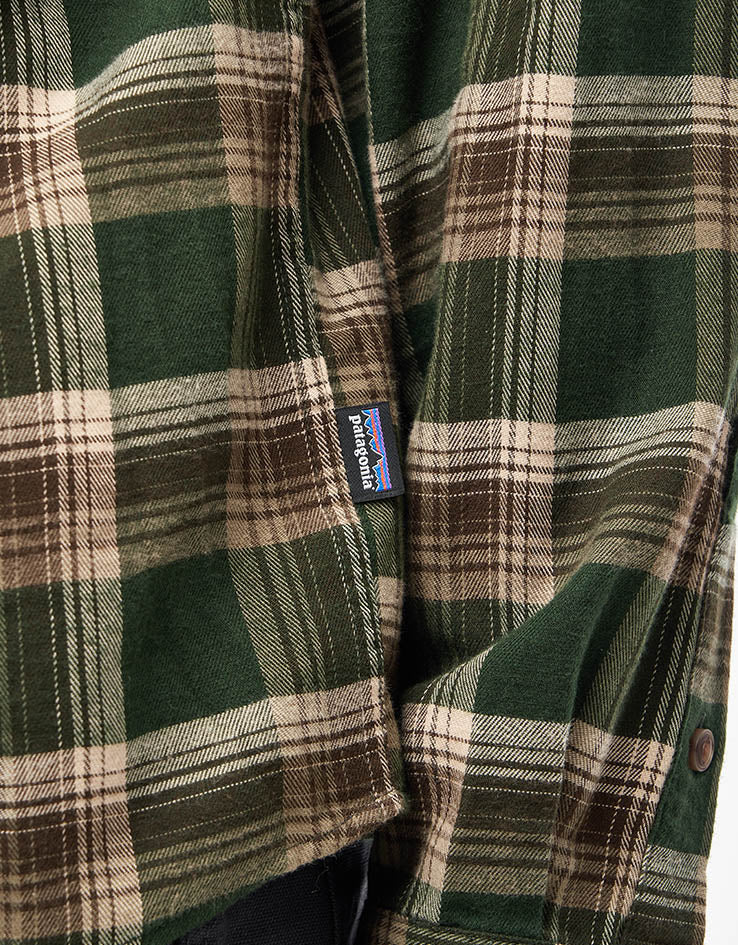 Close-up detail of a plaid flannel shirt pocket with small brand label, green and brown tartan pattern