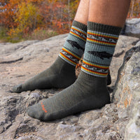 Crew-length wool hiking socks with trout motif and striped pattern, worn on rocky outdoor surface