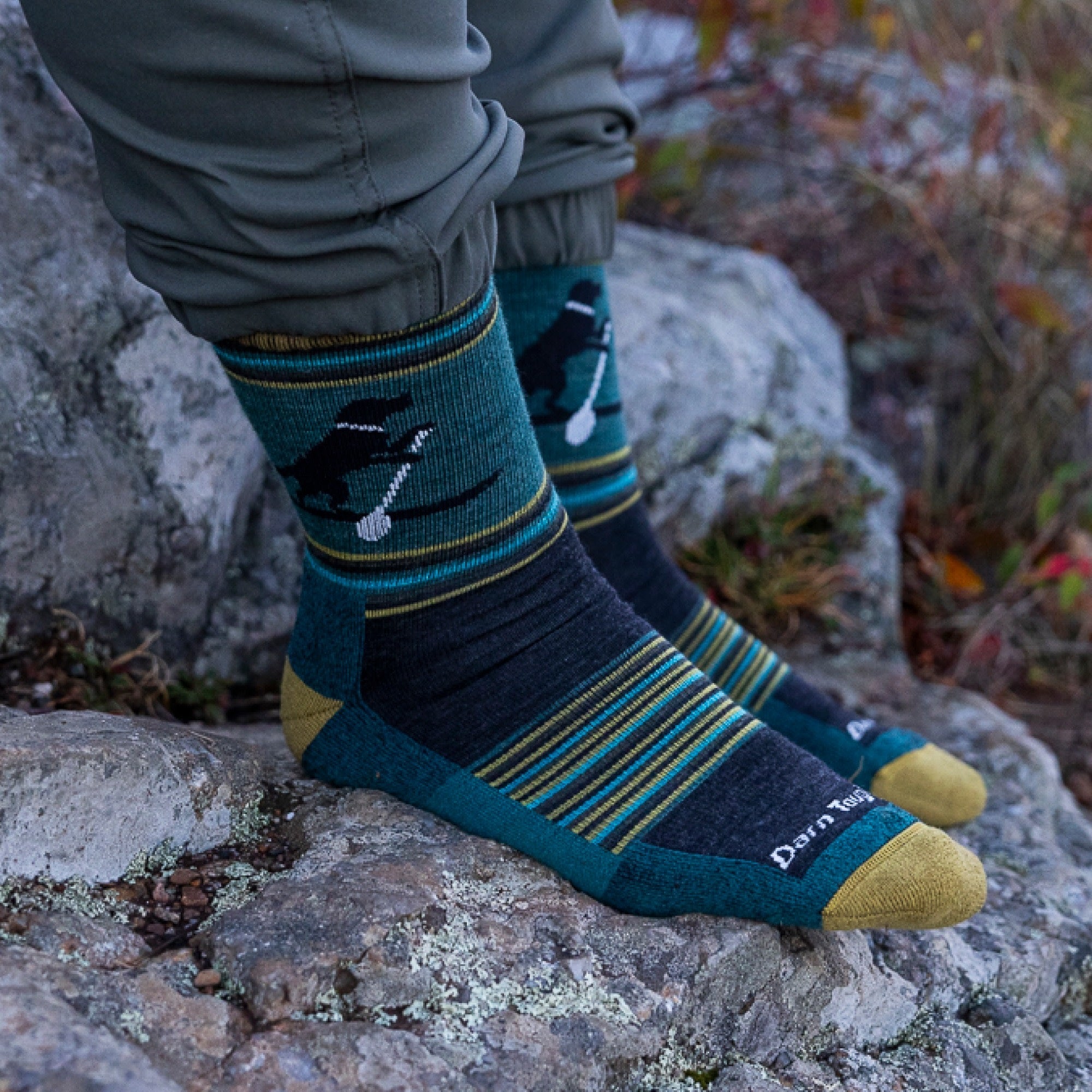 Crew-length wool socks with dog and paddle pattern, worn on rocky outdoor surface