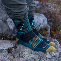 Crew-length wool socks with dog and paddle pattern, worn on rocky outdoor surface