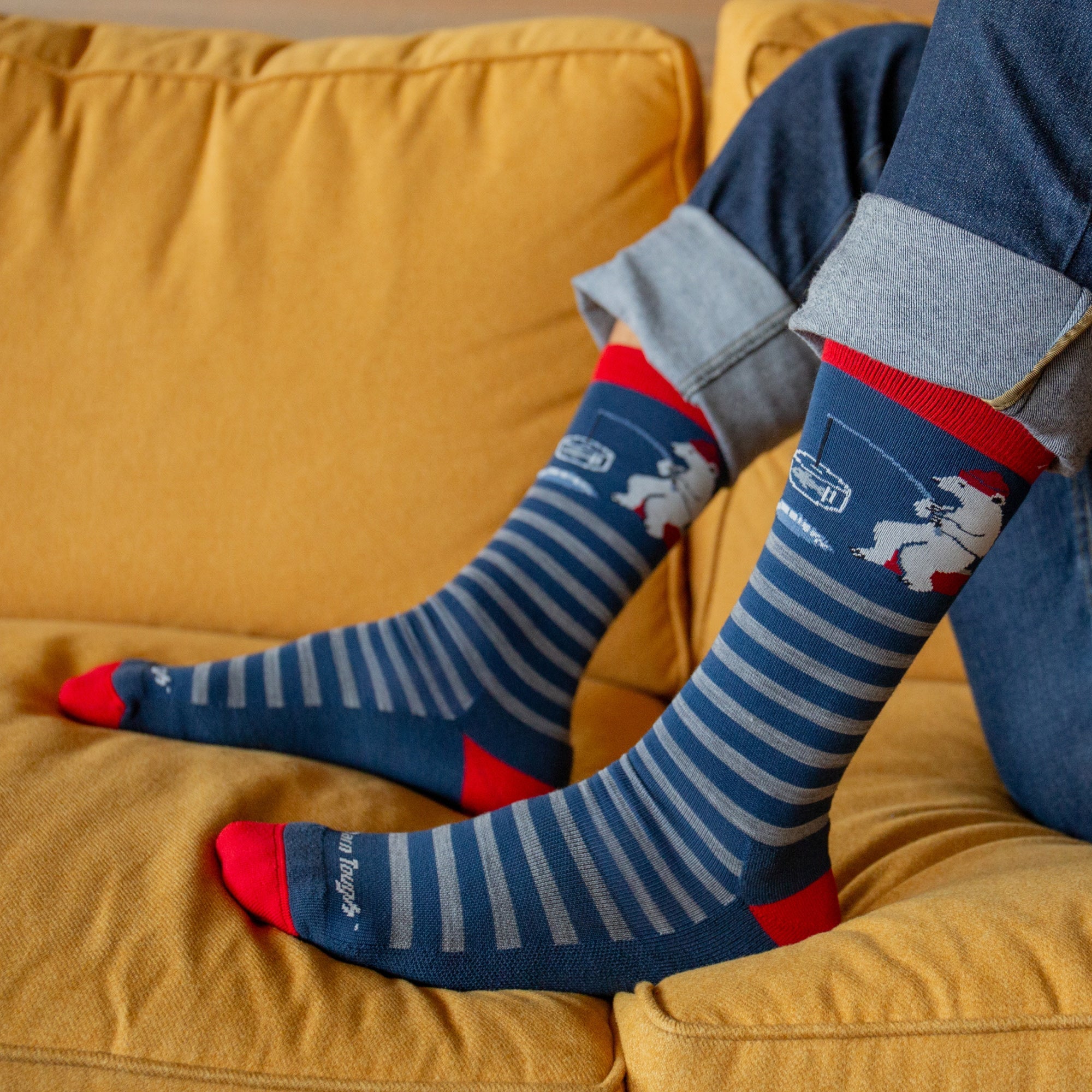 Navy striped crew socks with red accents and polar bear graphics, worn on model seated on yellow sofa