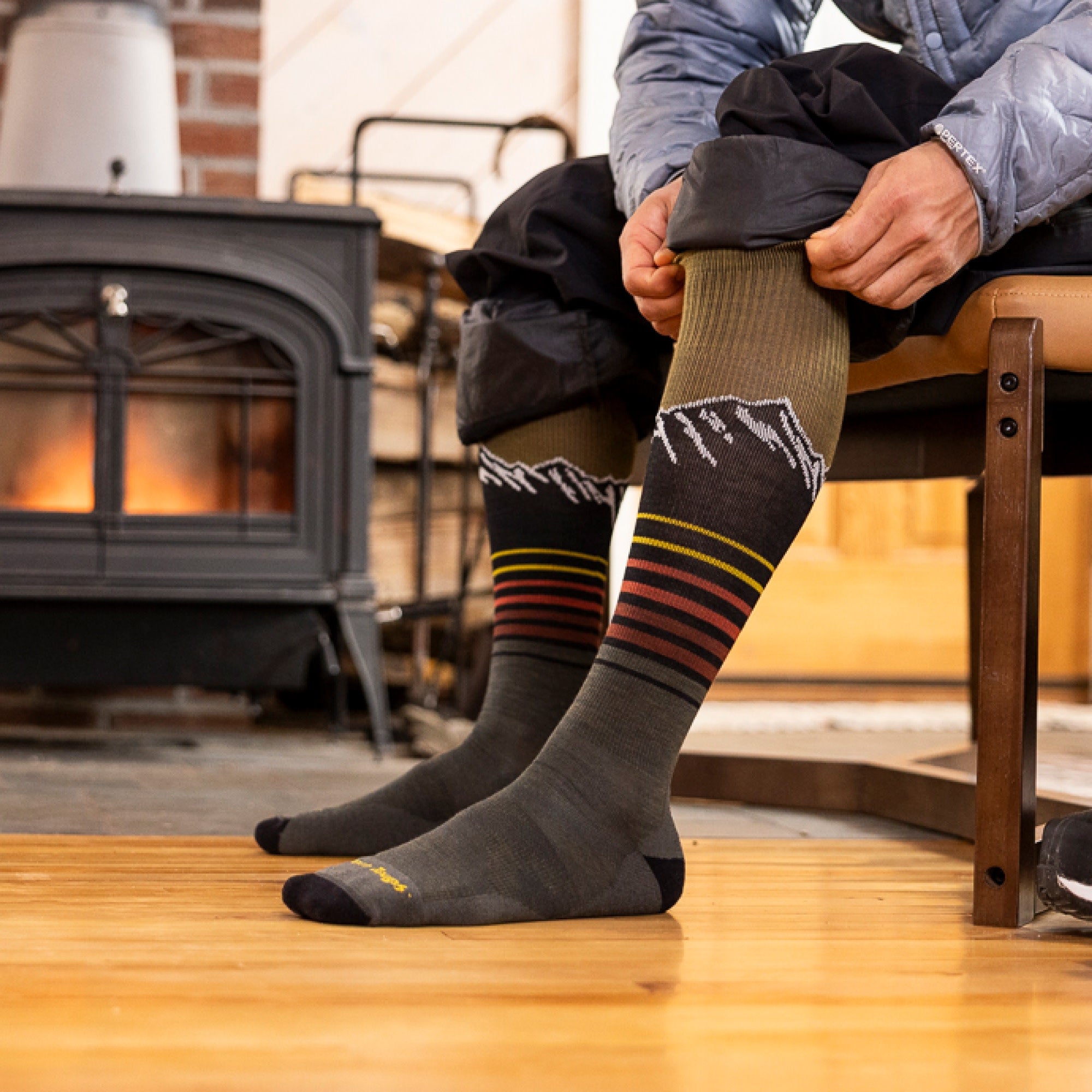 Over-the-calf wool socks with mountain peak design and colorful stripes, worn near wood stove