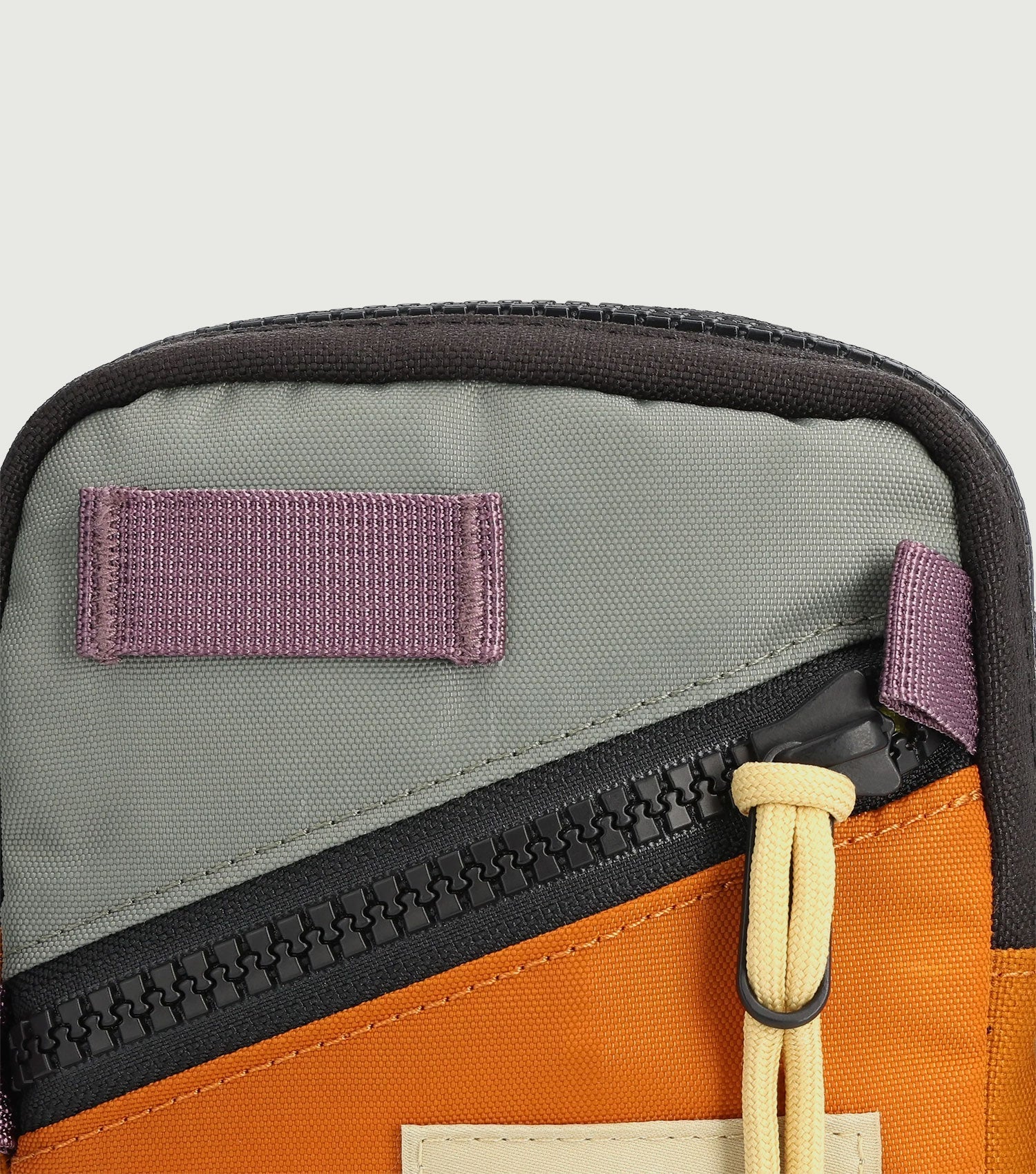 Mini shoulder bag with olive exterior, orange interior lining, and purple velcro patches, detail view
