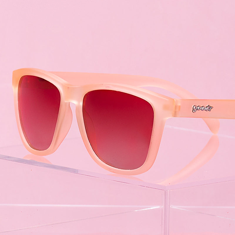 Translucent peachy pink sunglasses with red gradient lenses on clear acrylic display stand