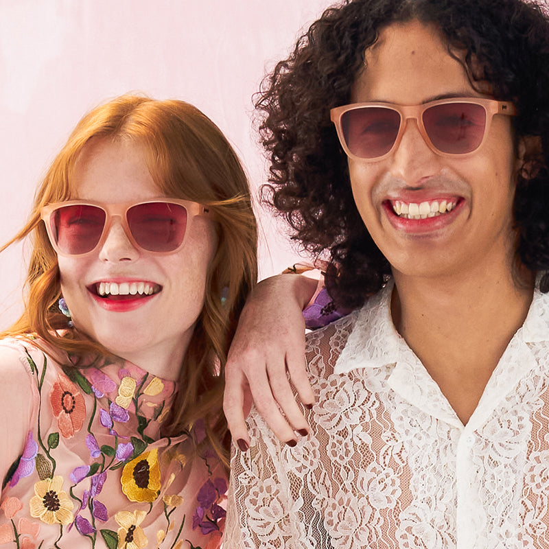 Two people wearing pink-framed sunglasses, smiling at camera in lifestyle photo