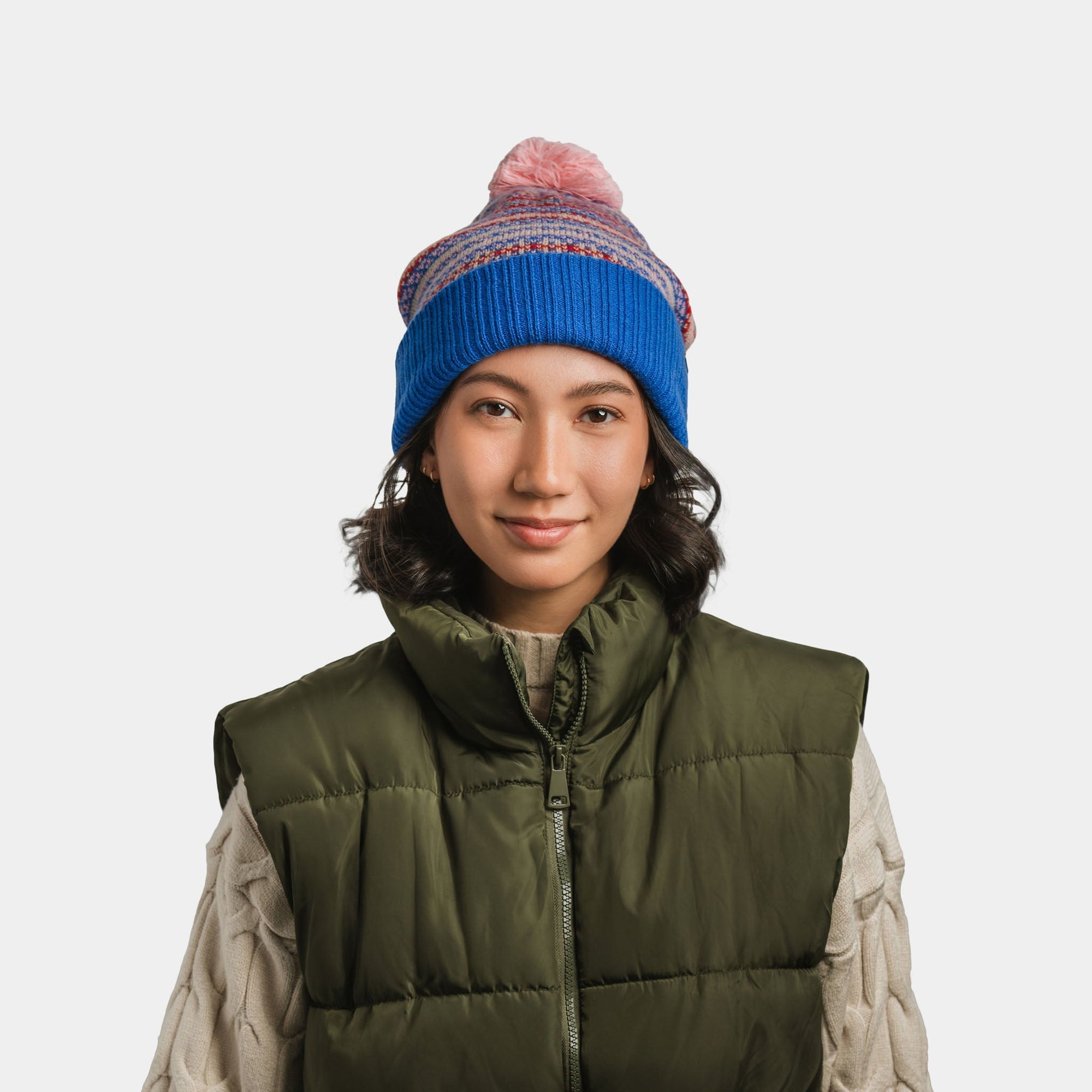 Knit pom-pom beanie in blue with colorful striped pattern, worn on model, front view