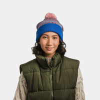 Knit pom-pom beanie in blue with colorful striped pattern, worn on model, front view