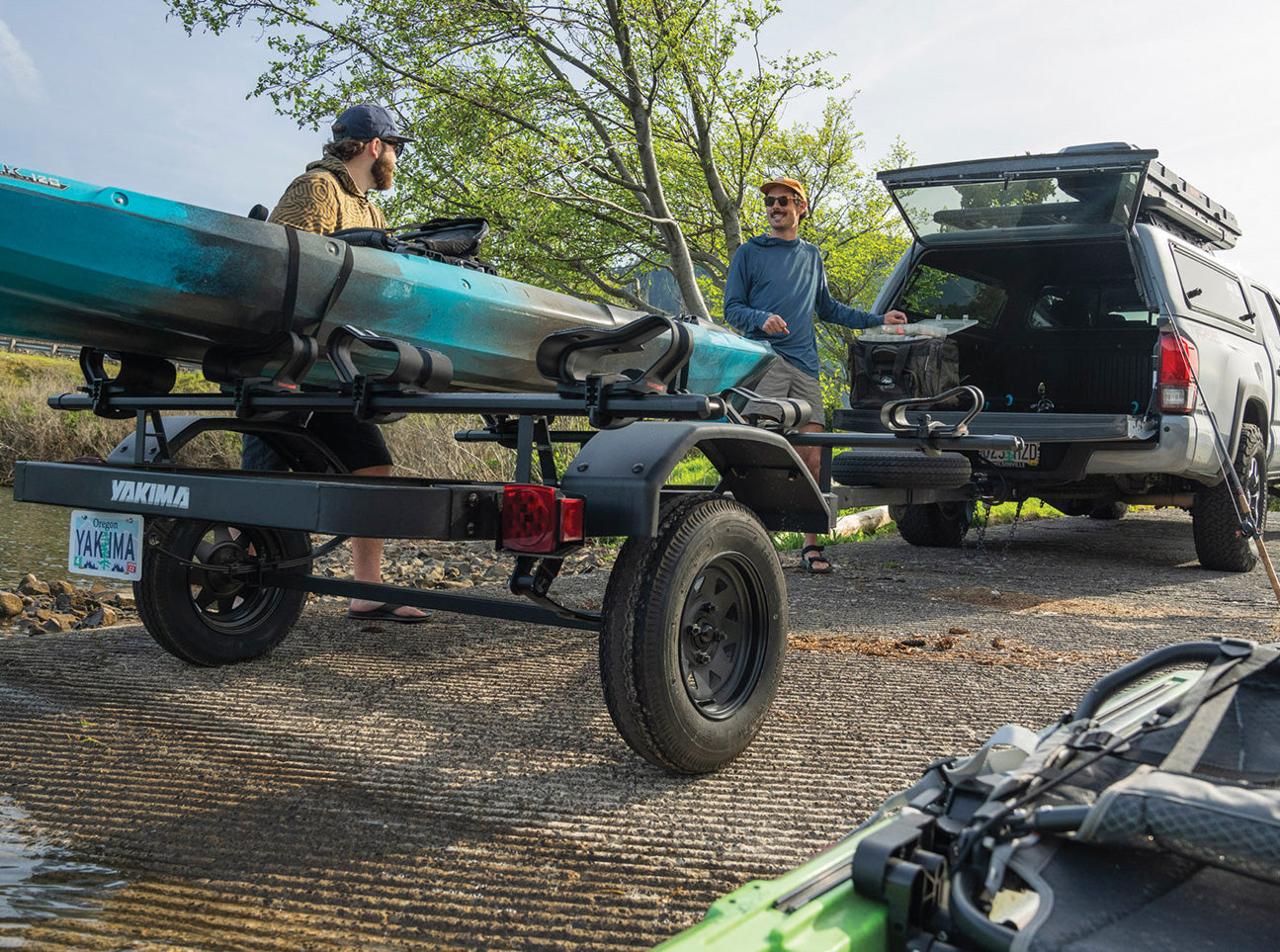 Black kayak trailer with two wheels carrying turquoise kayaks beside pickup truck
