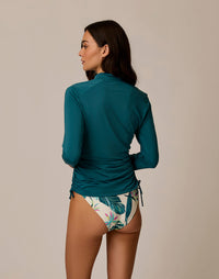 Women's long-sleeve rashguard in deep teal with ruched sides, back view, paired with floral bikini bottoms