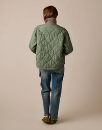 Back view of quilted reversible jacket in sage green with small print, paired with jeans