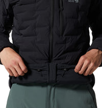Close-up detail of black quilted down jacket showing hem adjustment cord and zip, on model