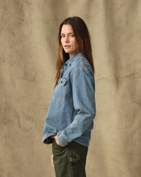 Women's light blue denim shirt with chest pocket, worn on model, side view