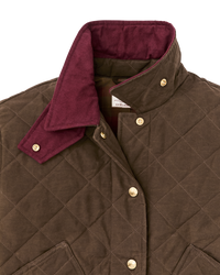 Quilted women's jacket close-up showing diamond stitching, snap buttons, and burgundy collar lining