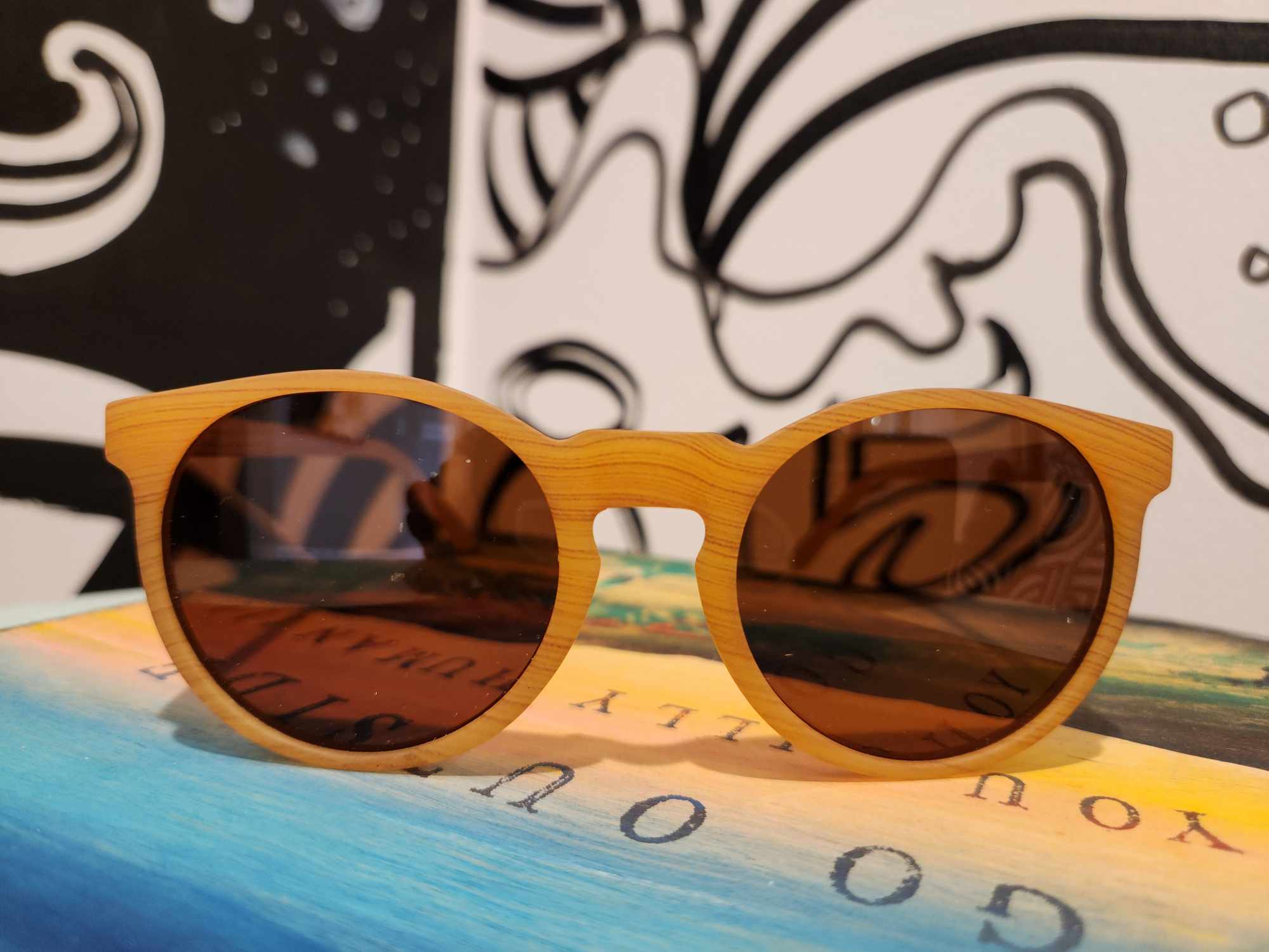 Round wooden sunglasses with amber lenses sitting on colorful surface with artistic background