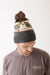 Pom-pom knit beanie with fish pattern, worn on model, gray cuff with olive and cream design