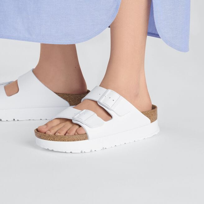 White platform sandals with dual buckle straps and cork footbed, worn by person