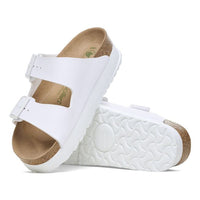 White two-strap sandals with cork footbed and white textured sole, angled view