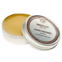Open round tin showing golden leather conditioning balm with lid displaying product label