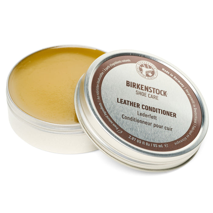 Open round tin showing golden leather conditioning balm with lid displaying product label