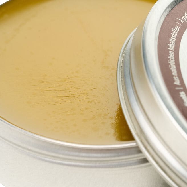 Open round container showing translucent yellow leather conditioning balm with smooth waxy texture