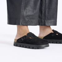 Black suede closed-toe clogs with buckle strap and chunky lug sole, on-model view