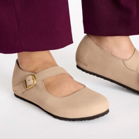 Light tan Mary Jane style shoes with ankle strap and gold buckle on feet
