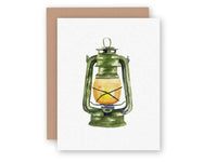 White greeting card featuring watercolor illustration of green vintage lantern with warm glowing light