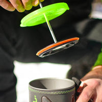 Silicone coffee press plunger being lifted from insulated camping mug, showing filter assembly