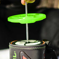 Green silicone coffee press plunger being inserted into a camping cooking system cup