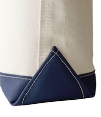 Close-up of canvas tote bag corner showing natural fabric with navy blue reinforced base