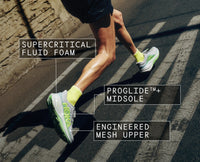 Runner wearing cushioned running shoes with neon green accents, mid-stride on crosswalk, featuring labeled technology callouts