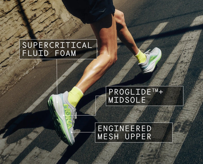 Runner wearing cushioned running shoes with neon green accents, mid-stride on crosswalk, featuring labeled technology callouts
