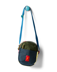 Round crossbody shoulder bag in colorblock navy and olive, hanging on a wall hook