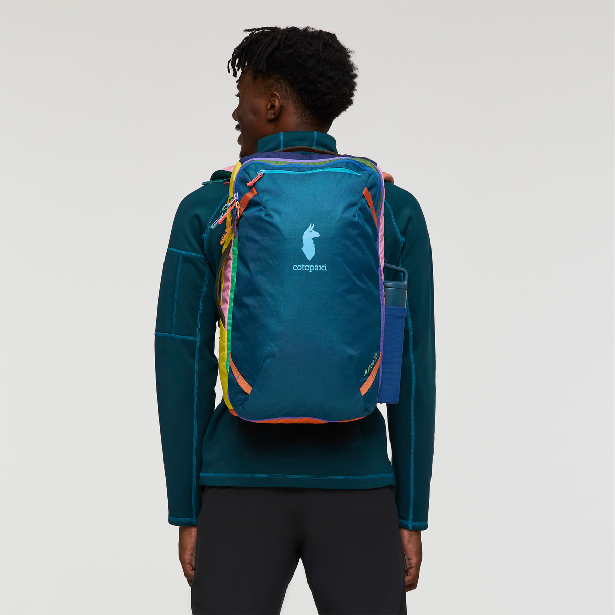Blue travel backpack with colorful rainbow straps worn by person, rear view