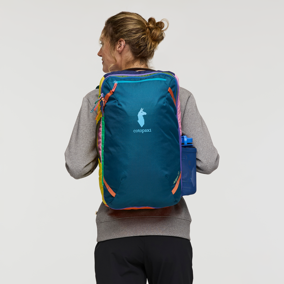 Teal travel backpack with colorful rainbow straps worn by person, back view