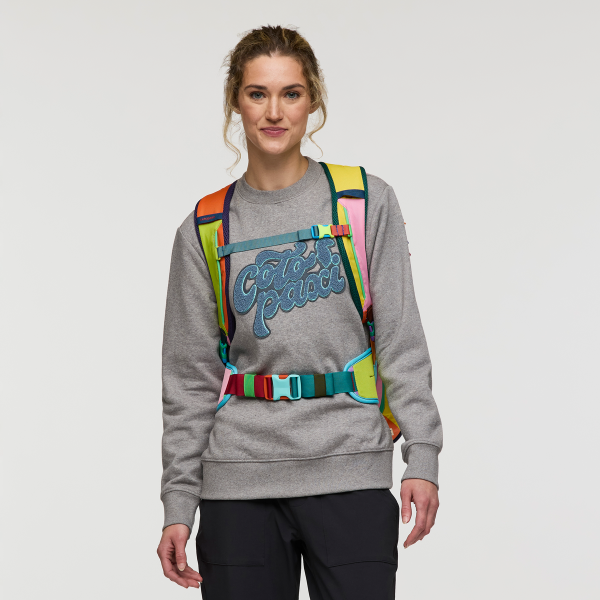Multicolored travel backpack with rainbow panels worn by woman in gray sweatshirt