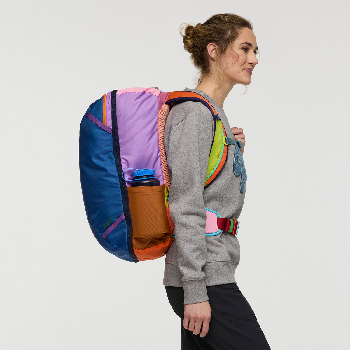 Colorful geometric patterned travel backpack worn by person, side profile view with water bottle pocket