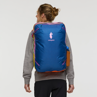 Blue travel backpack with rainbow striped accents worn by person, rear view showing logo