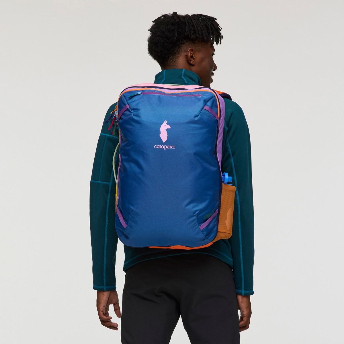 Multicolored travel backpack worn by person, rear view showing blue body with colorful accent panels