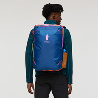 Multicolored travel backpack worn by person, rear view showing blue body with colorful accent panels