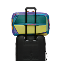 Colorful travel backpack with multiple mesh compartments open, shown on black wheeled luggage