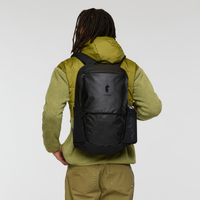 Black daypack backpack worn by person in olive green fleece, rear view showing design