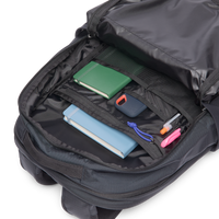 Black daypack with main compartment open showing books, external hard drive, and pens inside