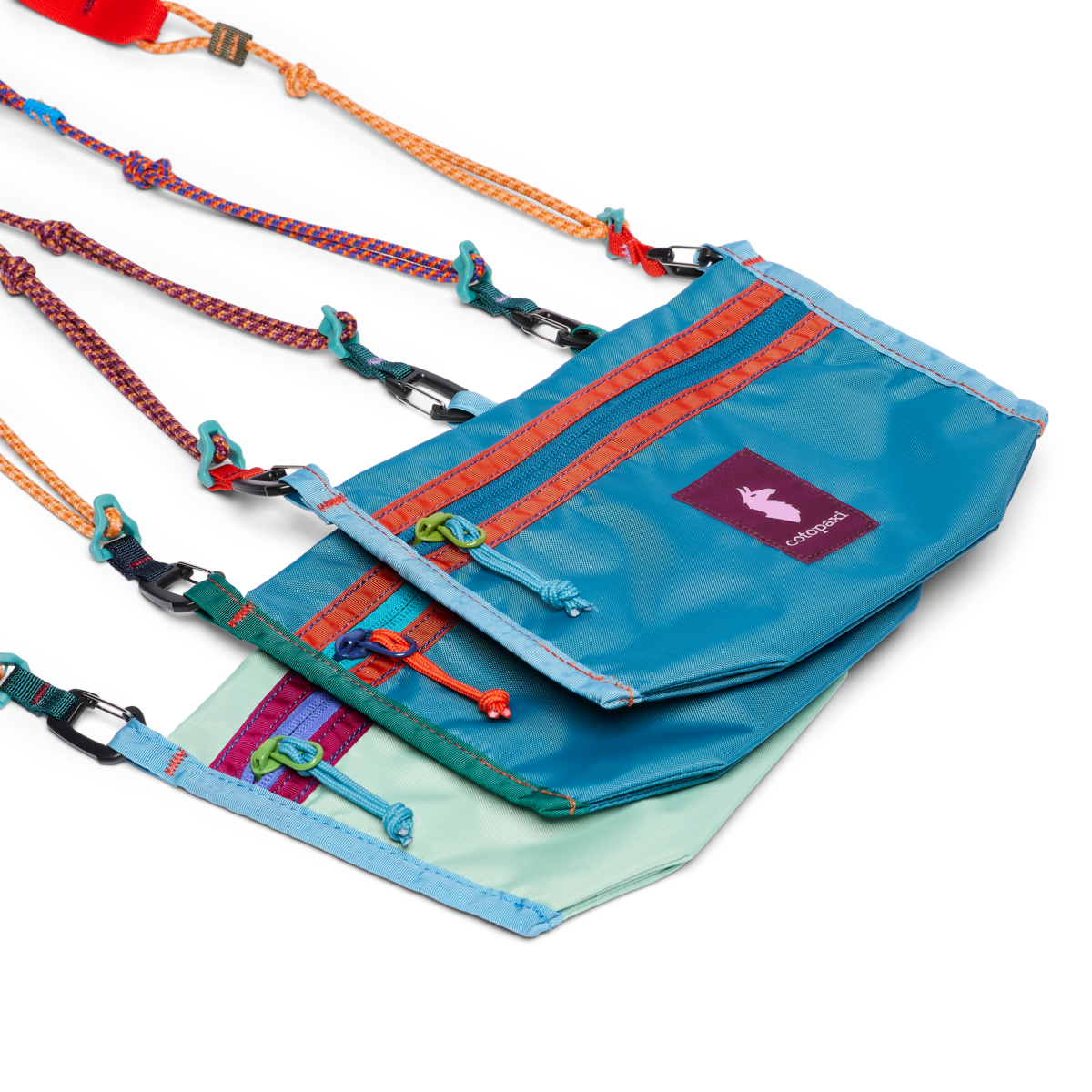 Three colorful crossbody bags with rope straps, zippers, and carabiner clips, stacked together