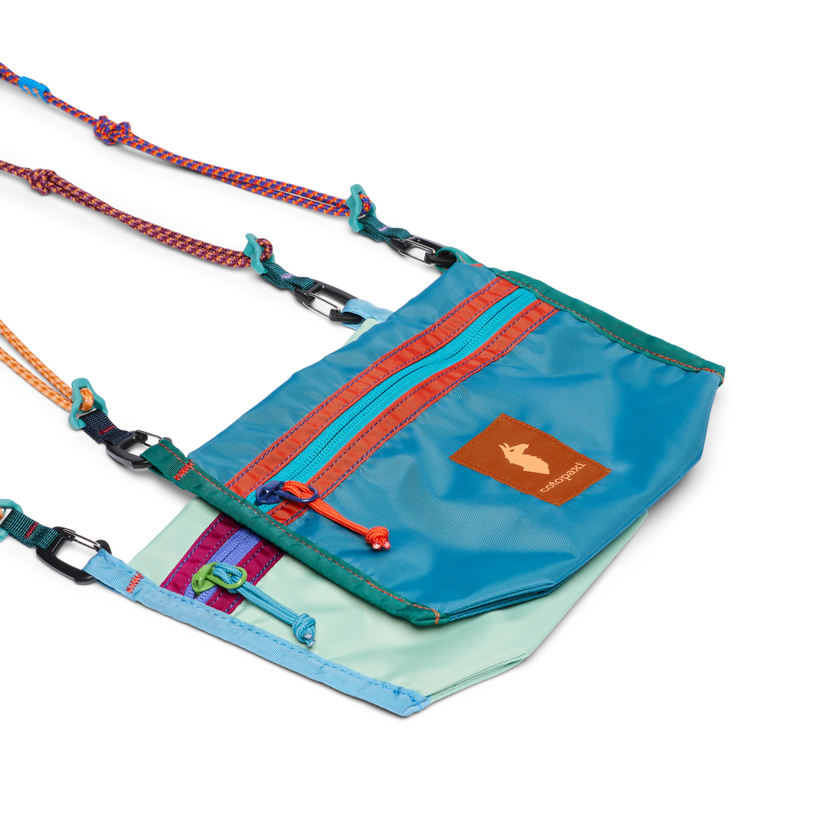 Small crossbody bag with teal exterior, front zip pocket, colorful straps, and carabiner clips
