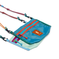 Small crossbody bag with teal exterior, front zip pocket, colorful straps, and carabiner clips