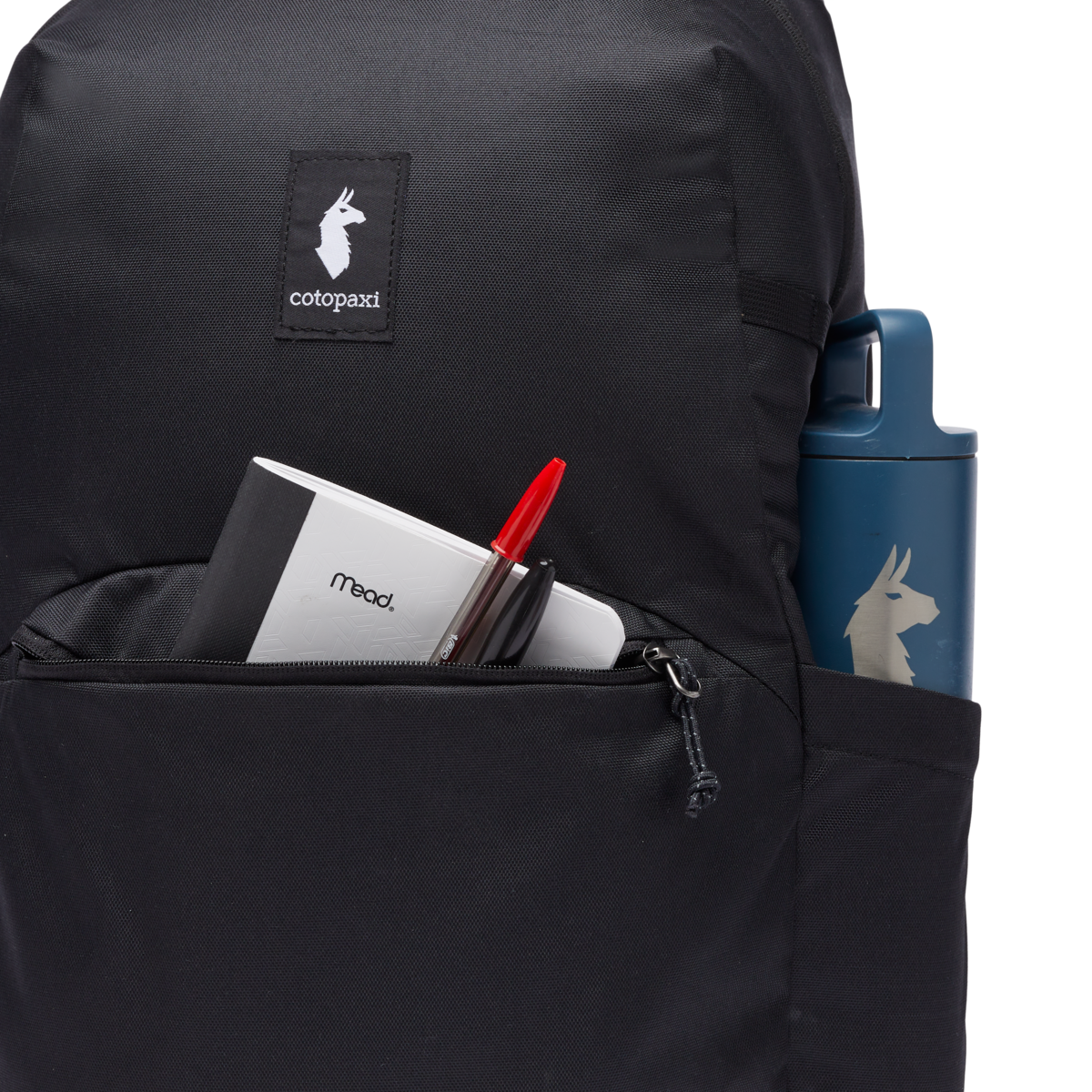 Close-up of black backpack front pocket with notebook, pen, and blue water bottle