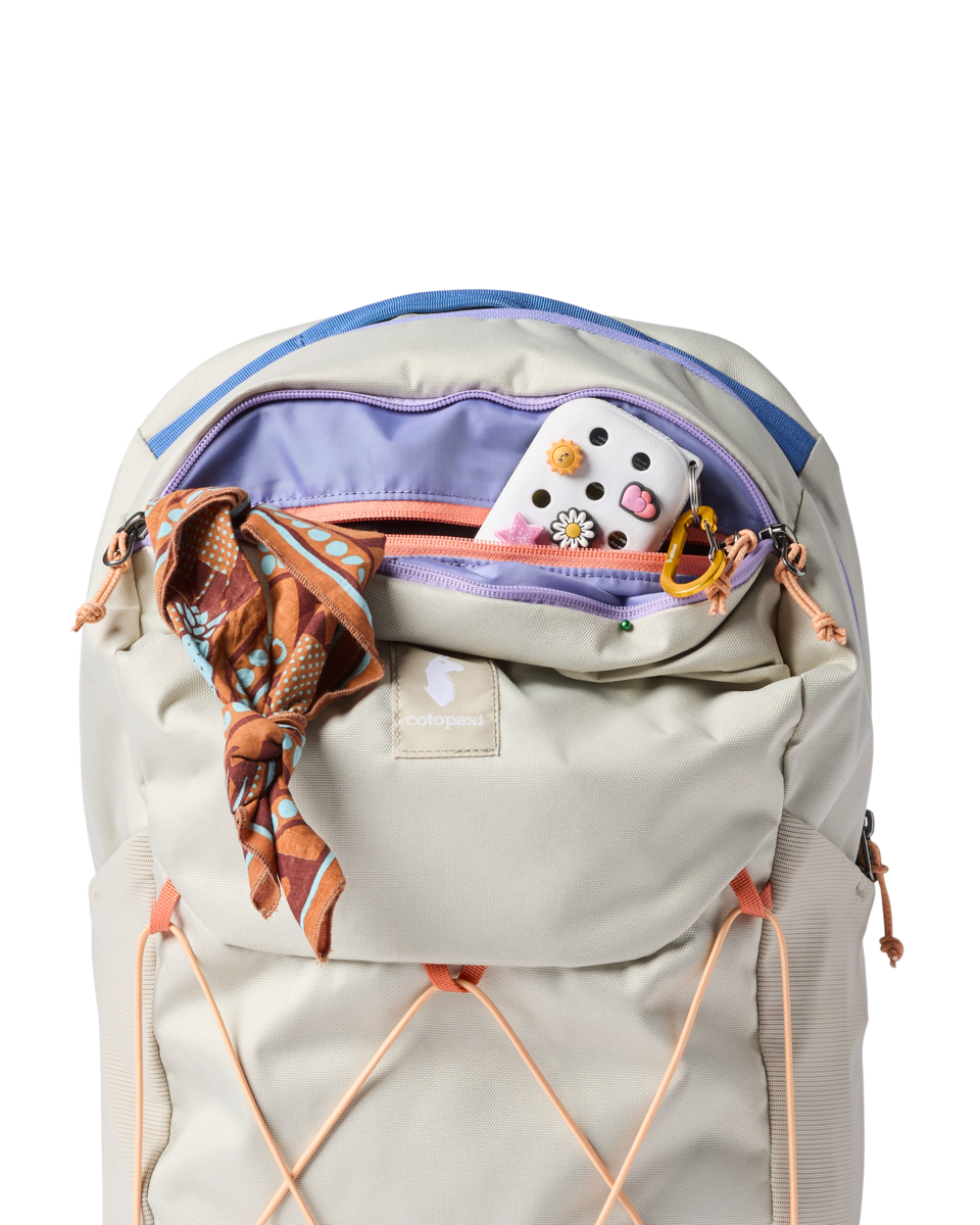 Light colored daypack with open main compartment showing interior organization and decorative items